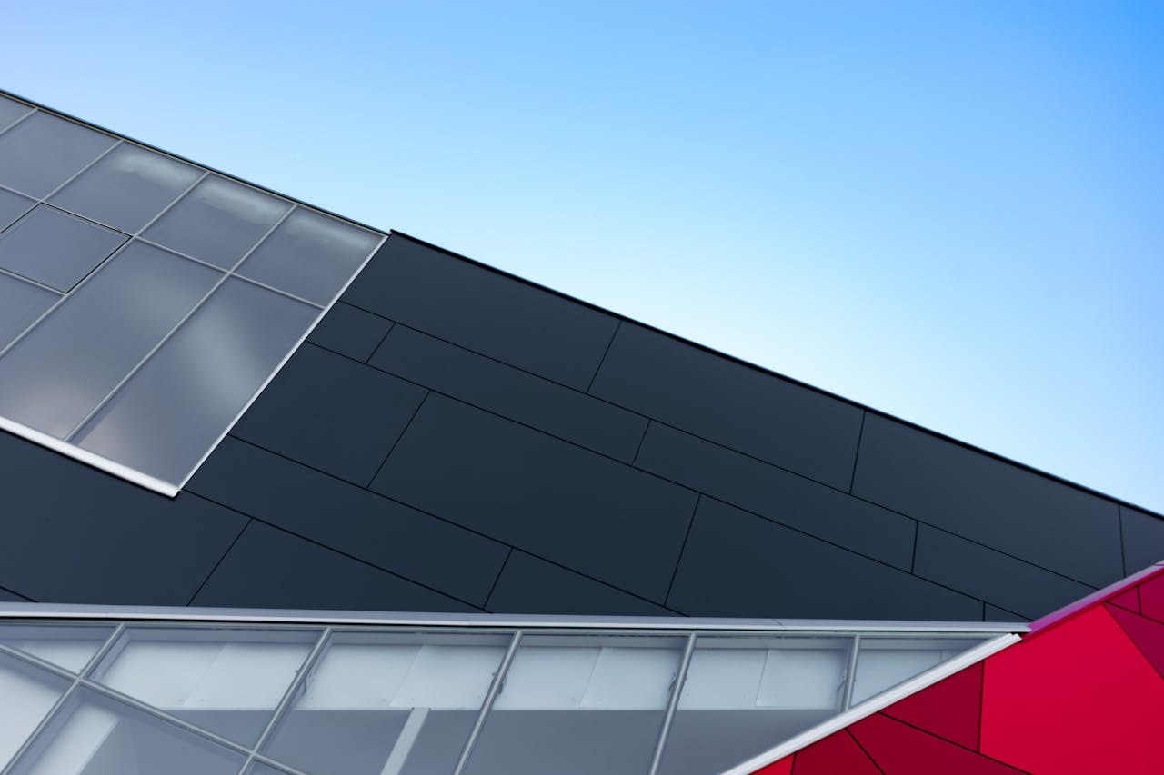 A modern building facade with geometric glass and steel patterns against a clear sky.